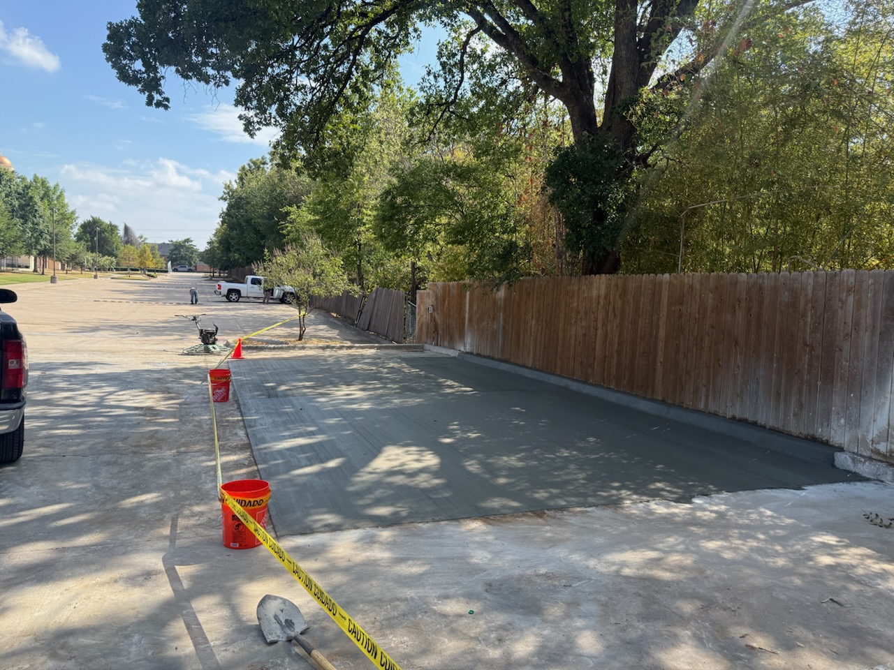 Fresh concrete parking extension beside a wood fence