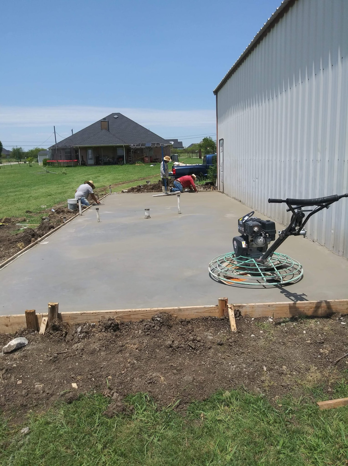Crew finishing a concrete slab beside a metal building
